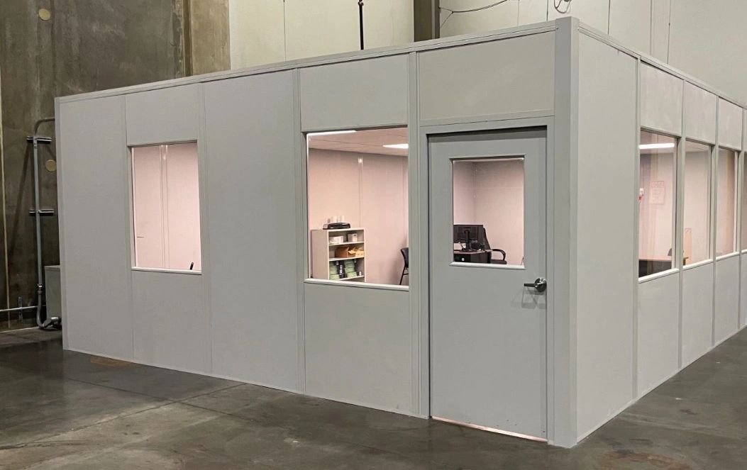 A clean, modern modular office building with multiple windows and a door, set up inside a large ware