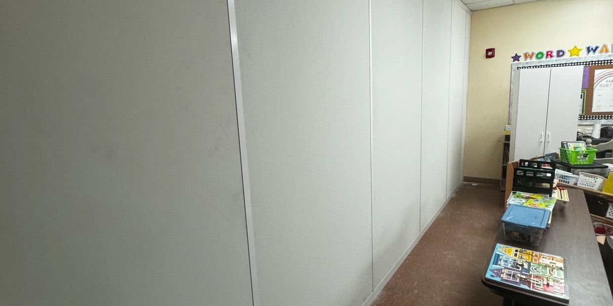 A white partition wall in a classroom setting. The wall stretches across the length of the room, div