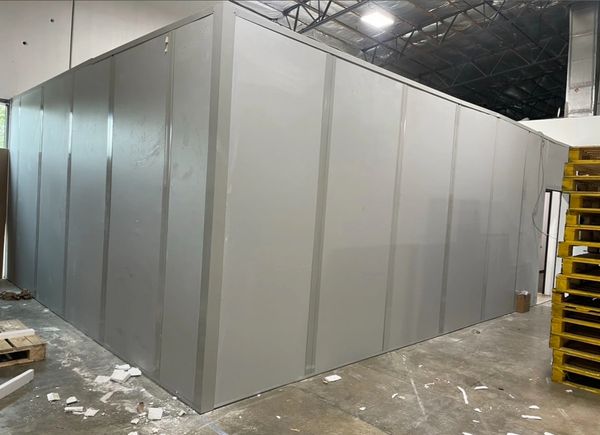 A large, modular powder coating room under construction inside a warehouse, with grey wall panels.