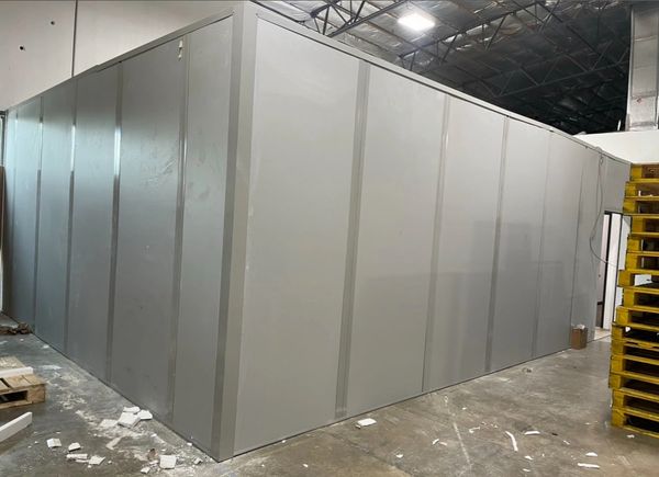 A modular, in-plant office with gray metal walls and a door in the corner. 