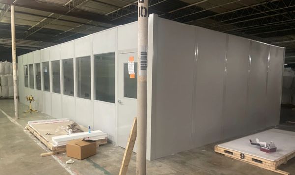 A prefabricated modular office building stands in a warehouse, ready for final installation inspecti