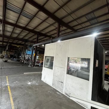 A small, white, modular office stands in the middle of a large industrial warehouse.