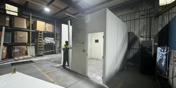 A worker installs a door on a prefabricated modular office unit inside a warehouse.