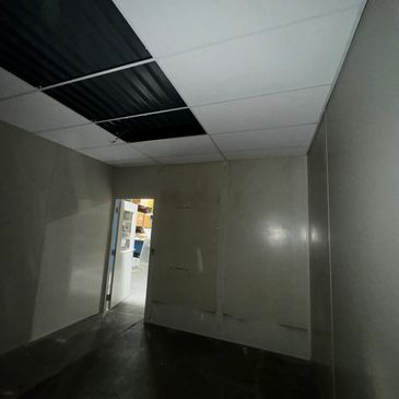 An empty modular office with a partially installed drop ceiling, featuring alternating white and bla