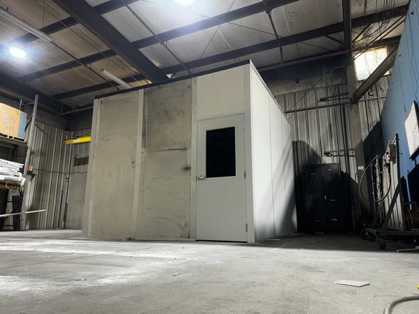 A prefabricated modular office with a single door and window, situated inside a large warehouse