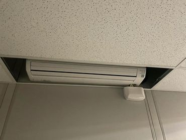 A ceiling-mounted air conditioner unit with its plug hanging down and plugged into a wall outlet.
