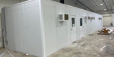 "A white modular office building by Starrco under construction inside a warehouse."
