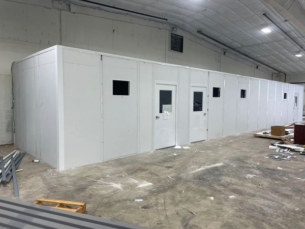 A large narrow white modular office solutions by SoFlo inside a warehouse settings with windows, doo