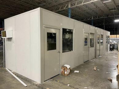 "A row of prefabricated modular office cabins within a larger industrial building."