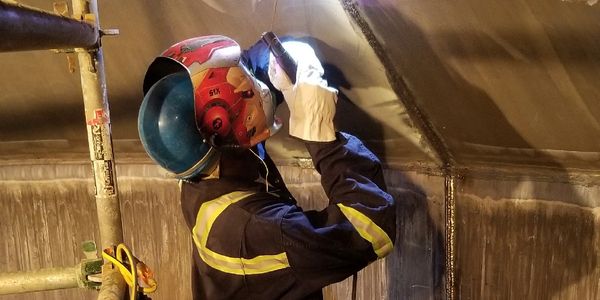 Worker welding metal with a protective helmet and gloves.