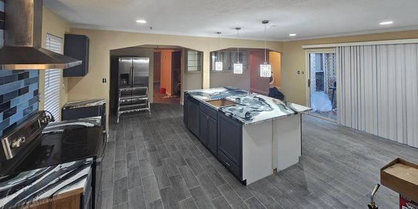 Modern kitchen under renovation with marble countertops and pendant lights.