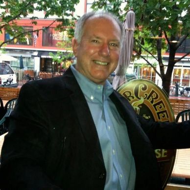 Smiling man in a blazer sitting outdoors.
