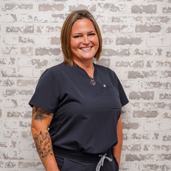 Smiling woman in black scrubs with arm tattoos.
