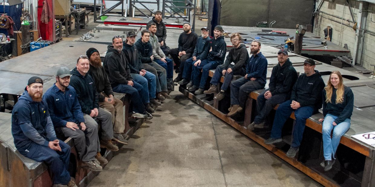 Group of workers seated on large metal structures in a warehouse.