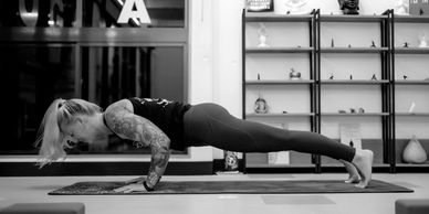 Woman performing low push-up in a yoga studio with tattoos visible.