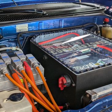 Close-up of a car's electric motor controller with vibrant orange cables.