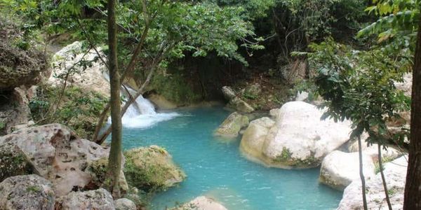 Tranquil turquoise waterfall surrounded by lush greenery and rocks.