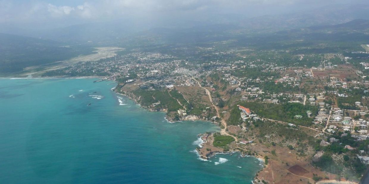 Aerial view of a coastal town with blue ocean and partly cloudy sky.