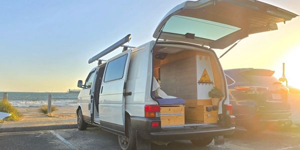 A camper van parked by the beach during sunset with its doors open.