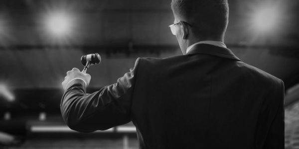 Man in suit holding a gavel, likely an auctioneer or judge.