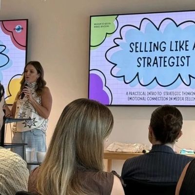 Woman speaking at a seminar on strategic selling with audience.