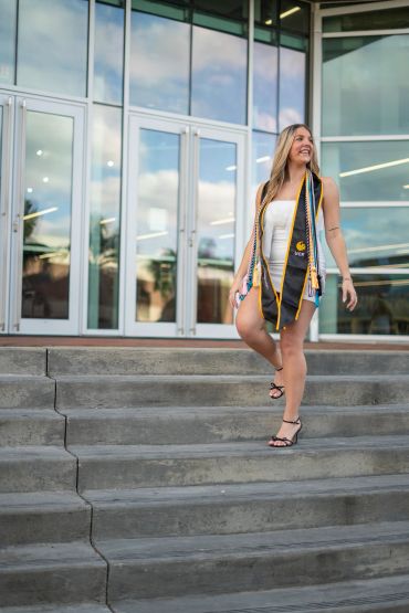 Young woman in graduation attire walking down steps with a smile.