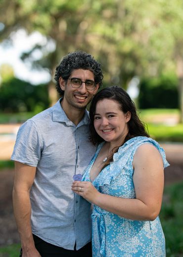 Smiling couple posing outdoors with greenery in the background.