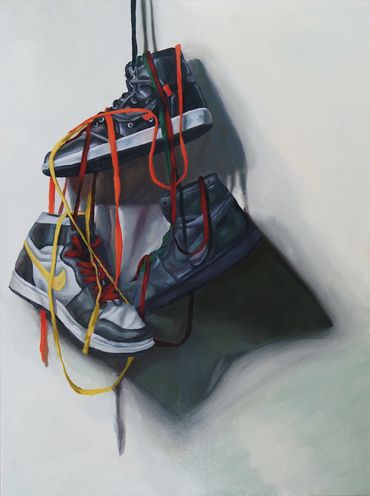 Three sneakers hanging by colorful laces casting shadows on a wall.
