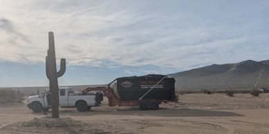 A white truck towing a large red and black trailer in a desert landscape.