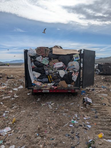A garbage truck overflowing with trash at a landfill.