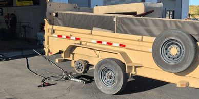 A beige utility trailer parked on a paved surface near buildings.