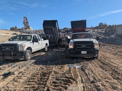Two dump trucks unloading debris at a landfill site under a clear sky.