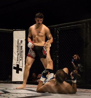 MMA fighter standing over opponent on the ground inside the cage.