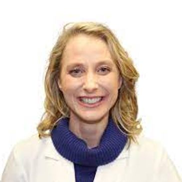 Smiling woman with blonde hair wearing a white coat and blue sweater.