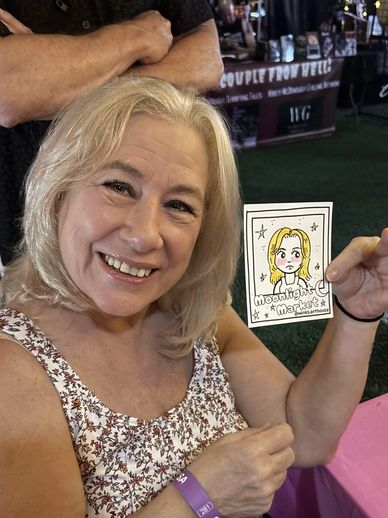 Smiling woman holding a cartoon portrait of herself at an event.