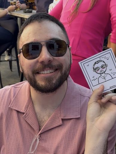 A smiling man in sunglasses holding a cartoon portrait of himself.