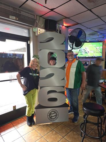 Three people posing with a large 2026 sign in a festive indoor setting.