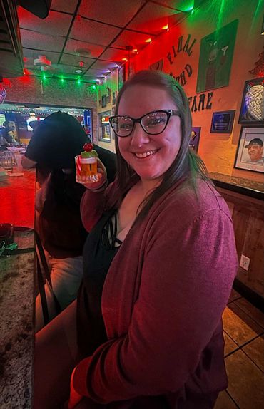 Smiling woman holding a cocktail in a cozy bar with colorful lights.