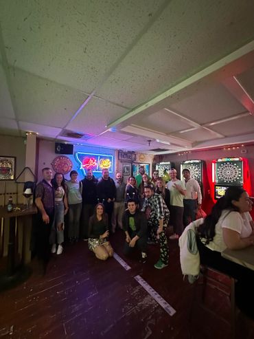 Group photo of people enjoying a night at a bar with neon lights and dartboards.
