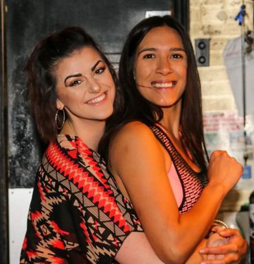 Two women smiling and hugging each other indoors.