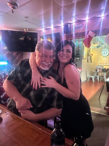 Two people smiling and hugging at a bar with festive decorations.