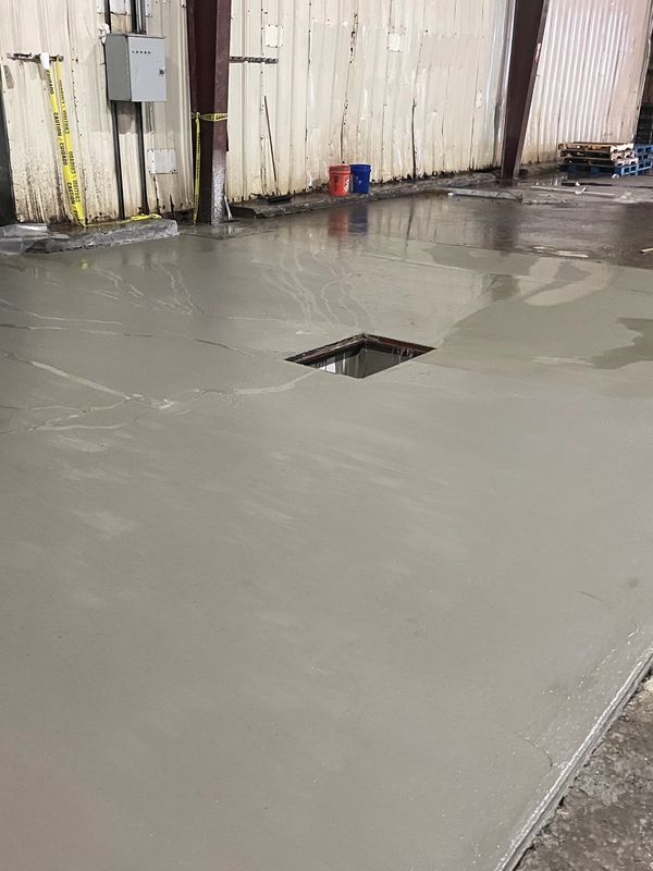 Freshly poured concrete floor inside an industrial building with a square opening.