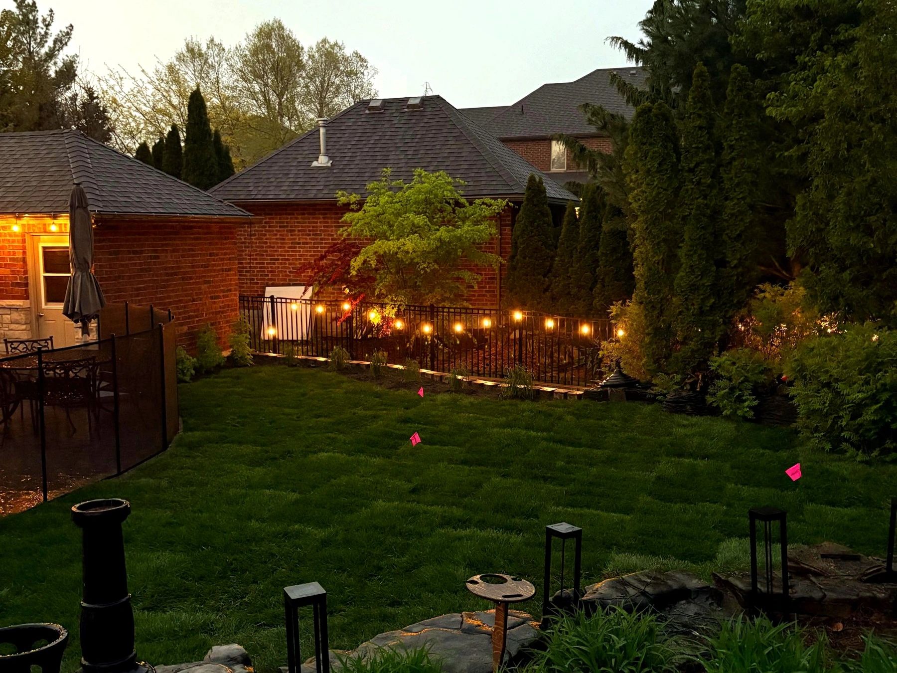 Backyard at dusk with string lights, lit garden beds and a new lawn