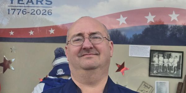 Man smiling in front of a patriotic mural.