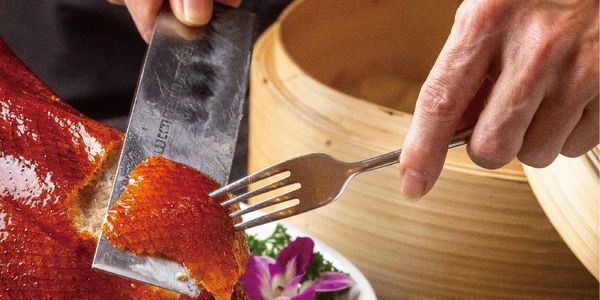 Chef slicing crispy Peking duck with a cleaver.