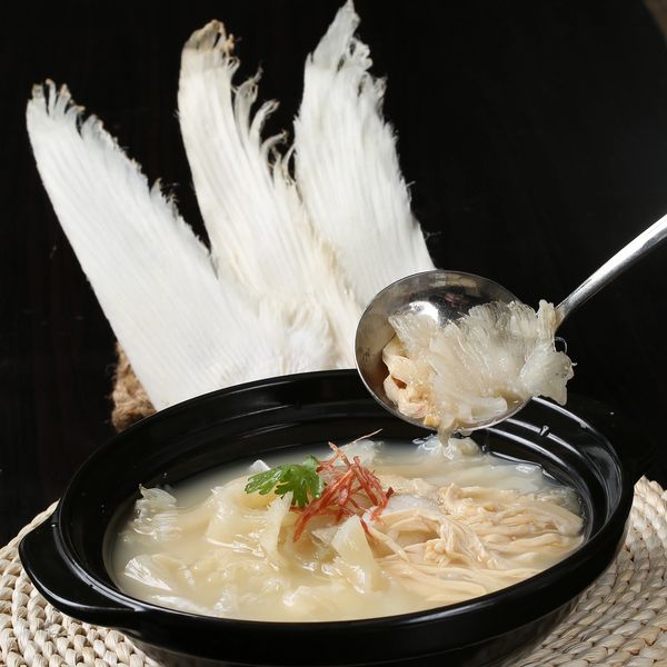 Black bowl of creamy soup with shredded ingredients and garnish, with white dried fish fins in background.
