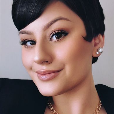 Close-up of a woman with short dark hair and pearl earrings, smiling softly.
