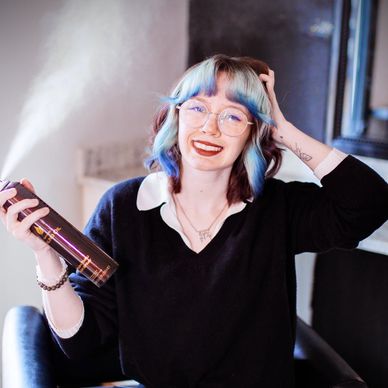 Smiling young woman with blue hair highlights holding a spray bottle.
