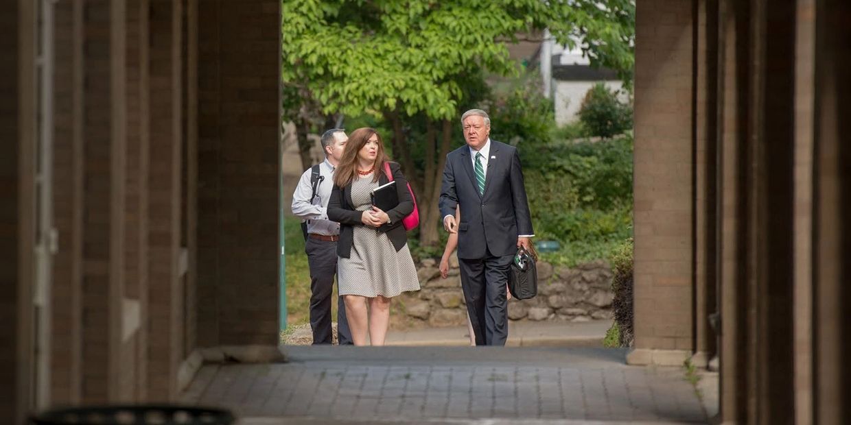 Three people walking outside through a brick archway.
