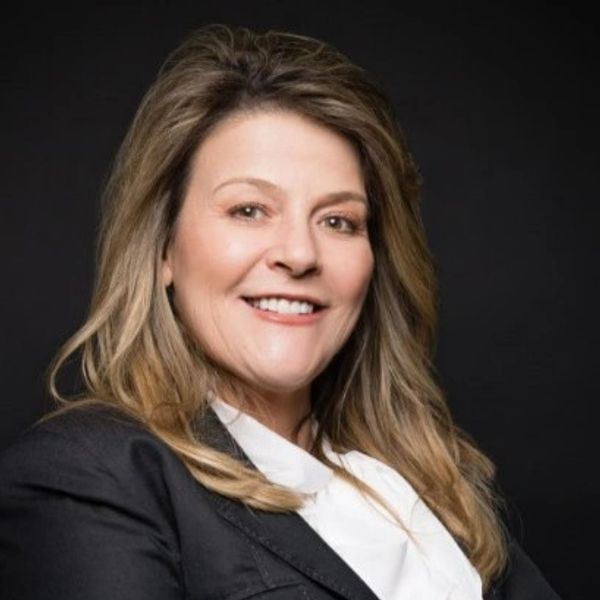 Professional woman smiling confidently in business attire against a black background.